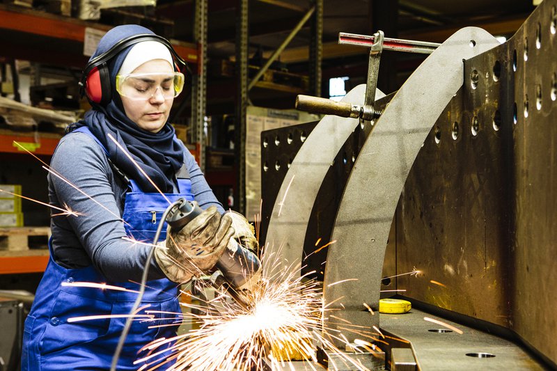 Young female trainee works with a grinder in a workshop